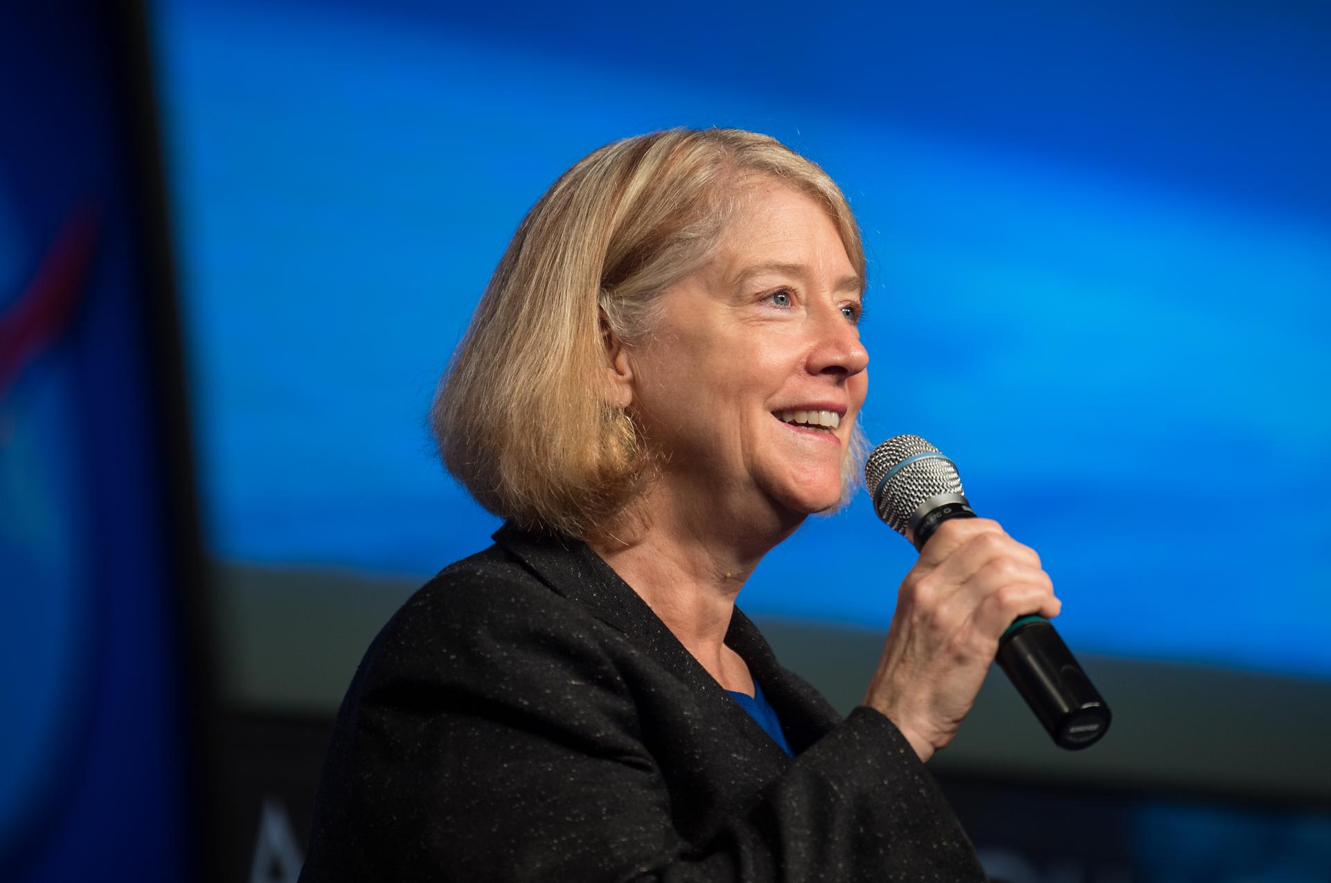 NASA Deputy Administrator Pam Melroy smiles as she speaks into a microphone at an employee town hall, with a blue background behind her.