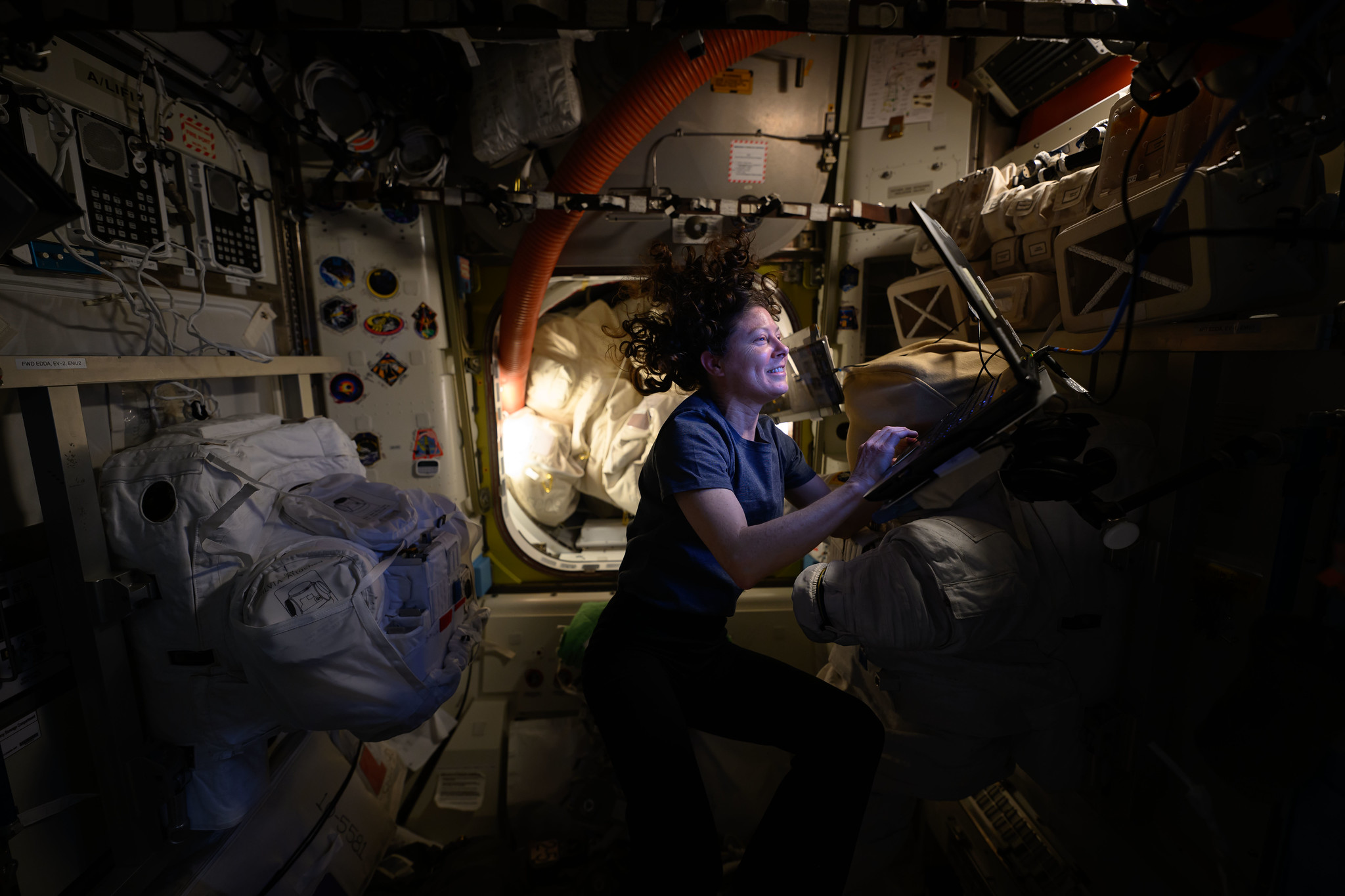 NASA astronaut Tracy C. Dyson, with floating hair and lit with the glow of a small lamp, smiles as she works at a computer station aboard the International Space Station.