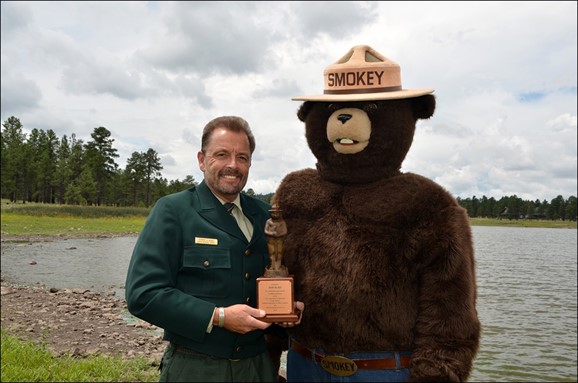 Title: Bob and Smokey - Description: Fire prevention specialist Bob Blasi accepts his award from Smokey Bear. 
Photo by Dyan Bone. Credit Kaibab National Forest.
