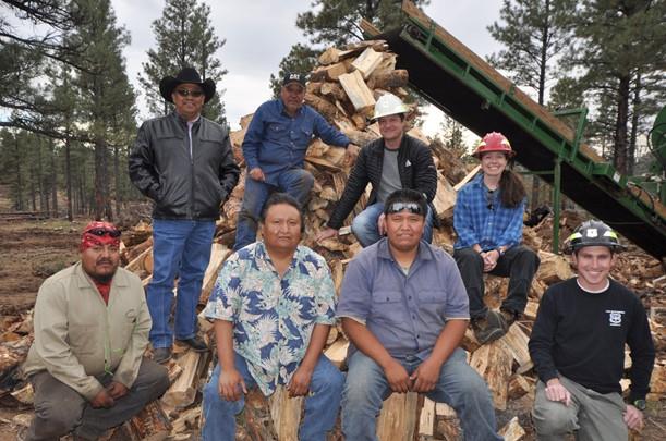 Title: Alamo Navajo Partnership - Description: Alamo Navajo and Kaibab National Forest representatives sit on a pile of firewood generated from forest restoration partnership efforts. Photo by Dyan Bone. Credit Kaibab National Forest.
